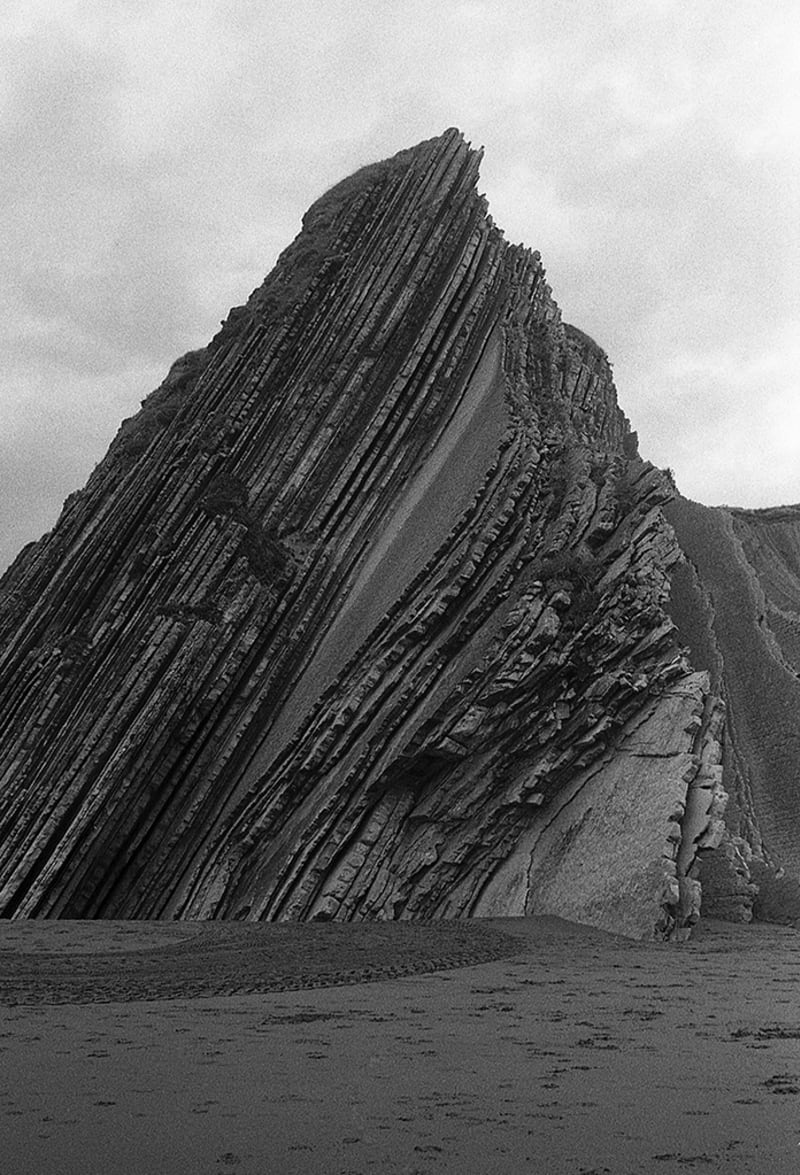 A girl with closed eyes and a big rock on a beach.