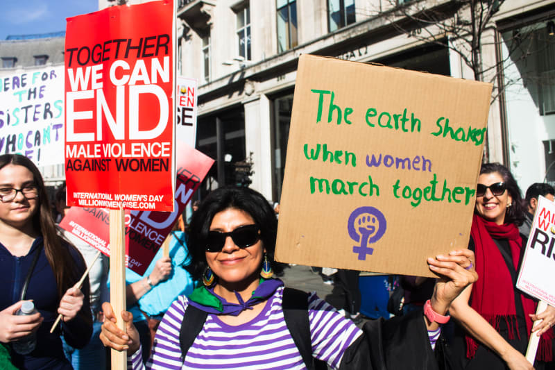 A march participant holding a "Million Women Rise" placard and a handmade cardboard sign reading "The Earth Shakes When Women March Together" 