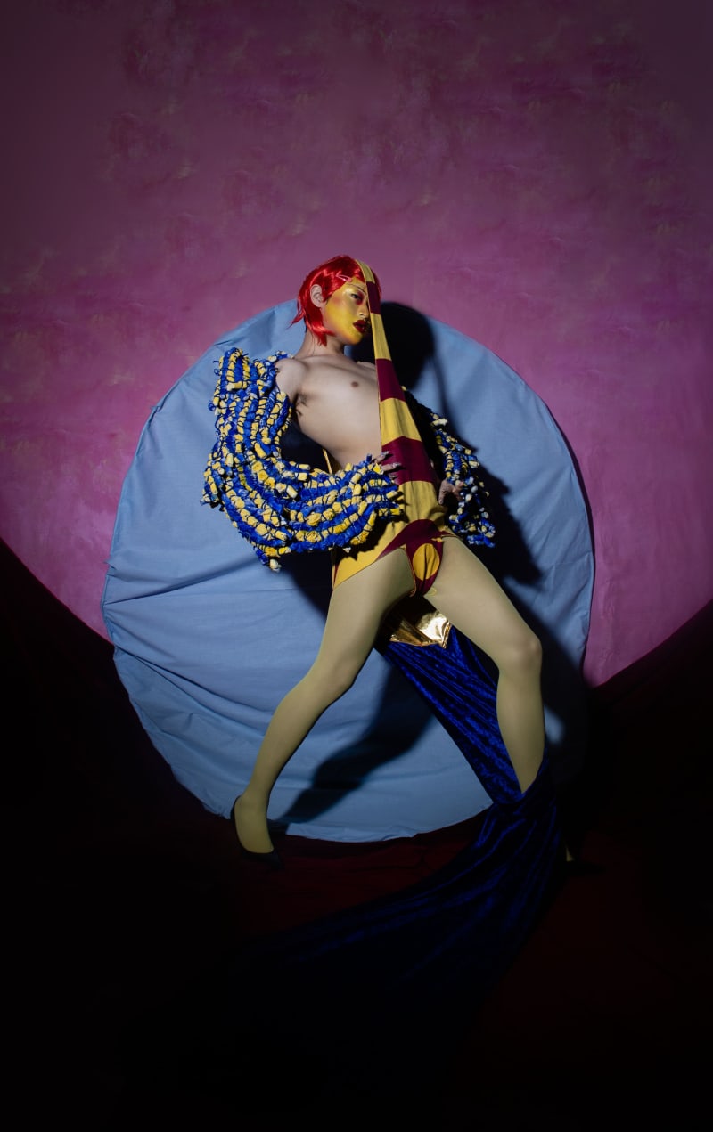 Figure standing in front of circular prop and pink backdrop