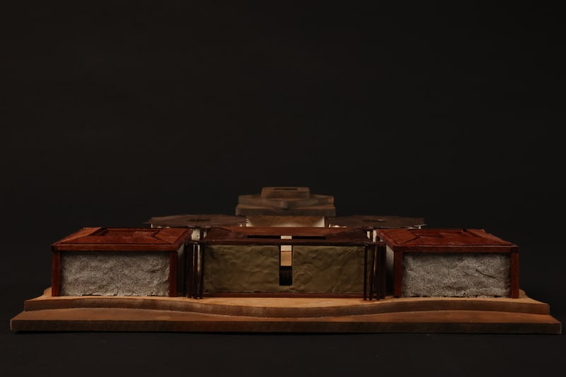 Frontal view of an architectural model featuring textured earthen walls, wooden roof structures, and layered platforms representing terrain.