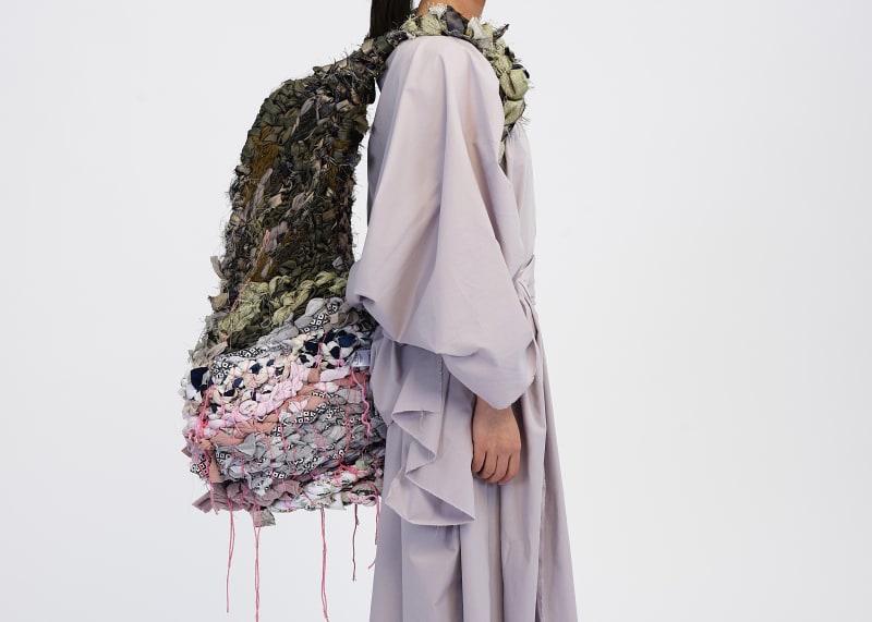 Side profile image of the backpack being worn on the body, showing how the basketry blends into the weave at the top of the structure.