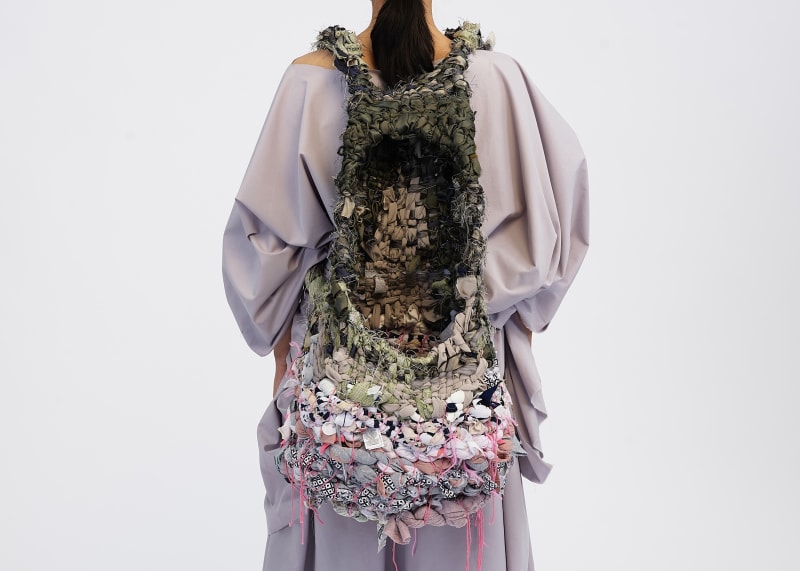 An image of the back of the backpack being worn on the body, displaying all of the weave techniques surrounding the opening and inside of the basket.
