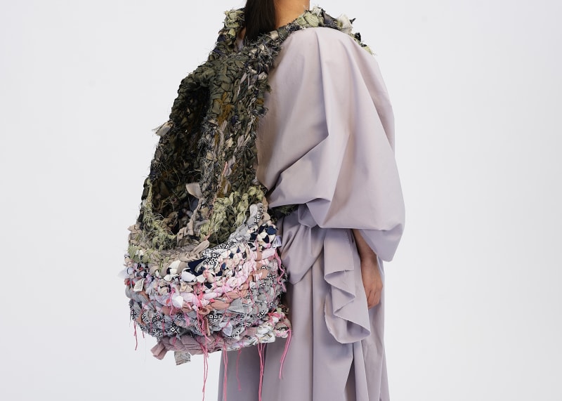 An image displaying the backpack being worn at an angle showing how the shape of it is reflected in the draped sleeve, yet there is still a contrast.