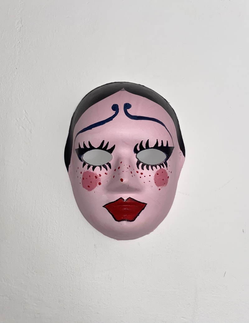A mask on a wall. Painted in pink. Resembling a face.