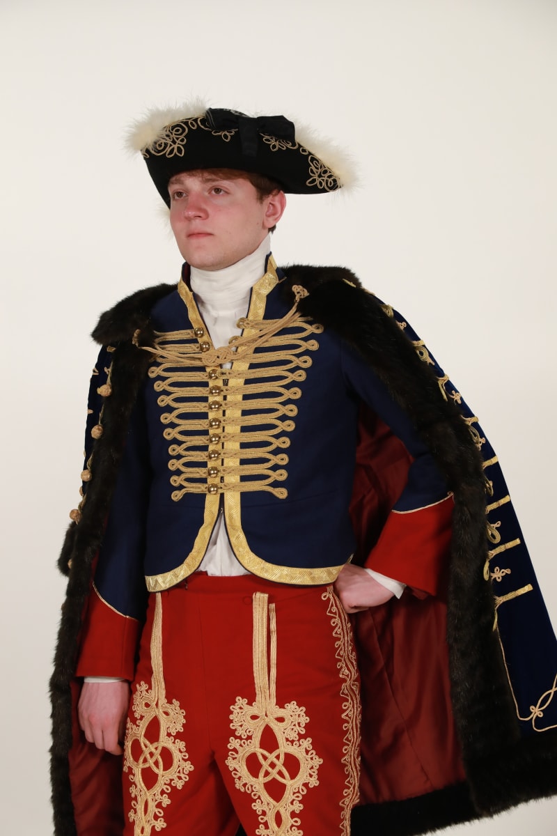 Photo of a man wearing a 19th century Hussar costume of deep blue and red with gold braiding accents.