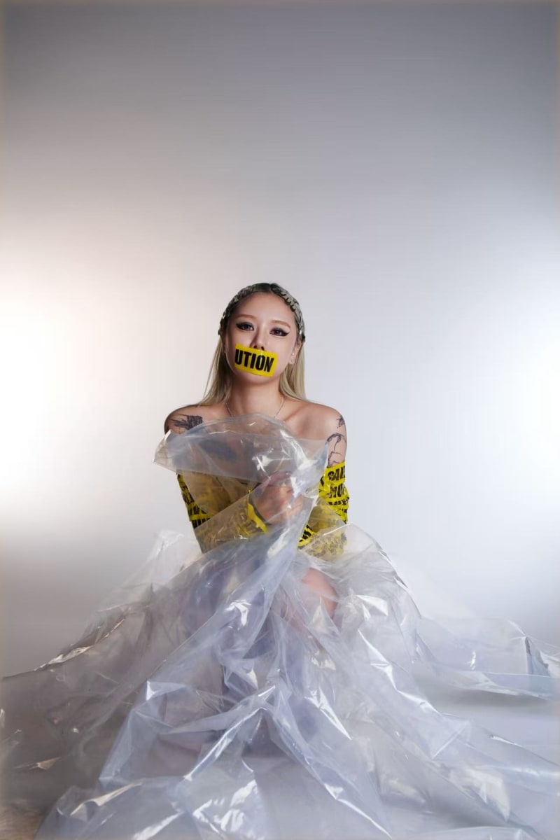 A woman is dressed in caution tape, and her mouth is covered by caution tape. 