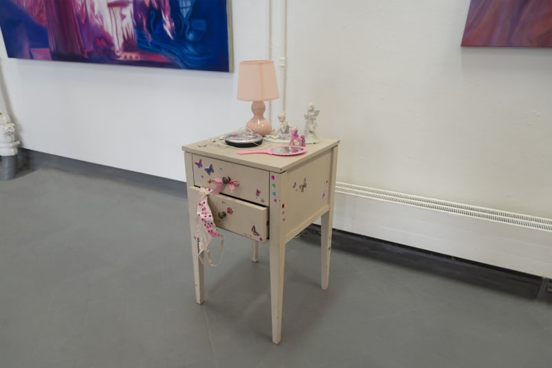 Stickered and bejewelled bedside table installation, atop lies a mirror, lamp, figurines and a bejewelled and stickered cd player.