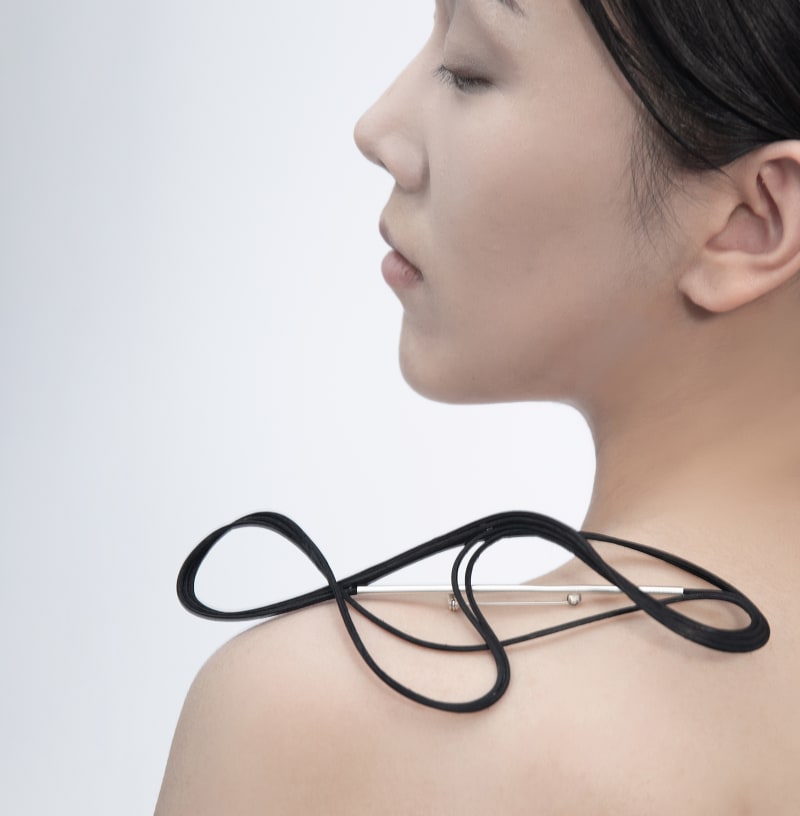 The brooch features rattan and silver tubes. The rattan pierces through the silver tubes and wraps around them, forming a smooth, flowing design aroun