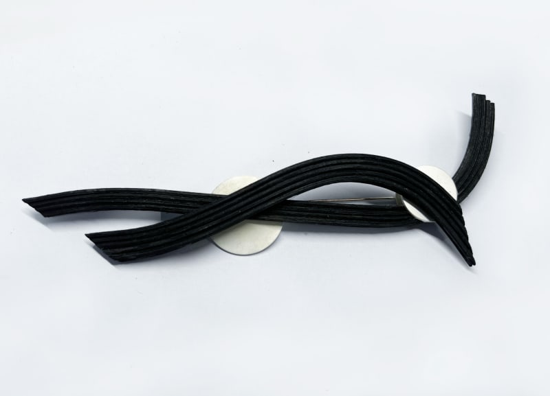 The long brooch features several evenly arranged rattan strips combined with a circular silver plate. The design highlights a clean, structured look w