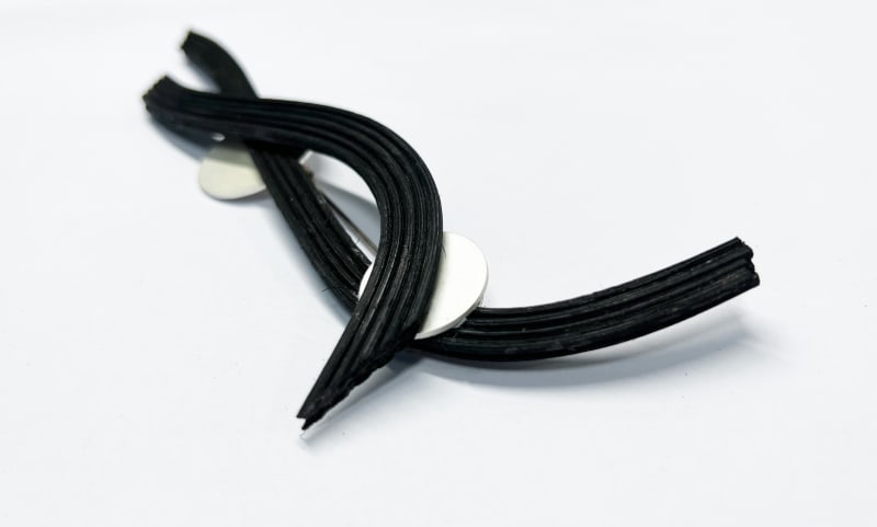 The long brooch features several evenly arranged rattan strips combined with a circular silver plate. The design highlights a clean, structured look w