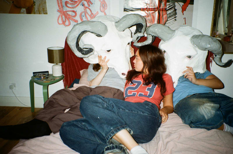 Two boys with large ram masks on a bed with a girl in a series of film photography.