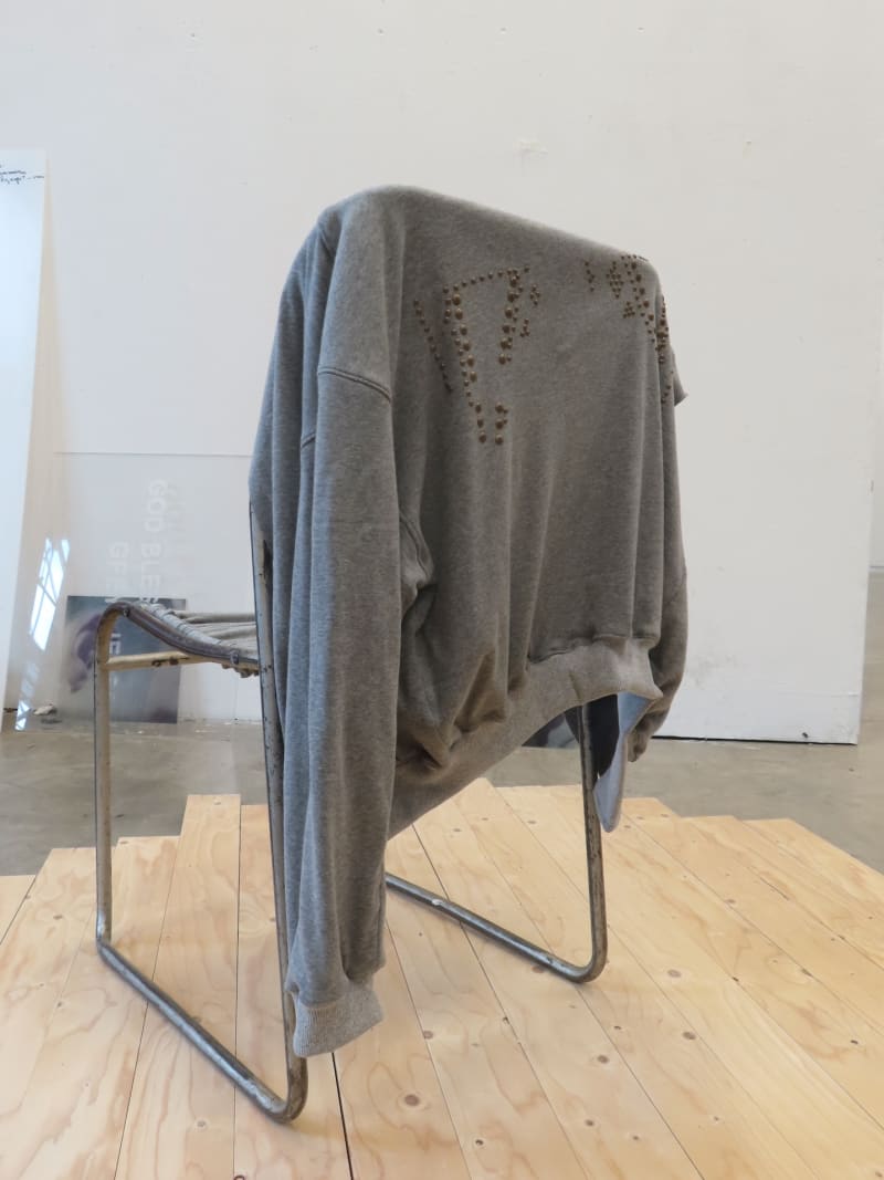 Grey pilot jacket with studs on the back made of sweatshirt fabric rests on the back of a metal school chair, upholstered in grey sweatshirt fabric