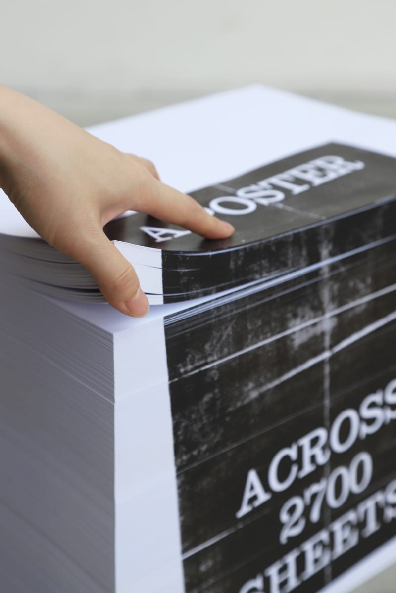 A single image is printed across the edges of 2,700 stacked sheets. As pages are lifted, the poster disappears—hidden within the paper’s thickness.