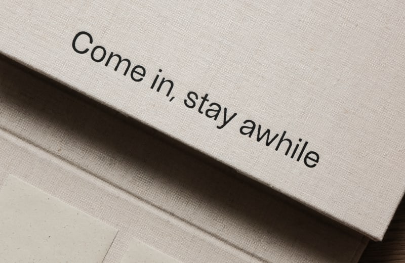 A linen-bound booklet opens to reveal layered pages, printed questions, and nostalgic photographs, exploring what makes us feel at home.
