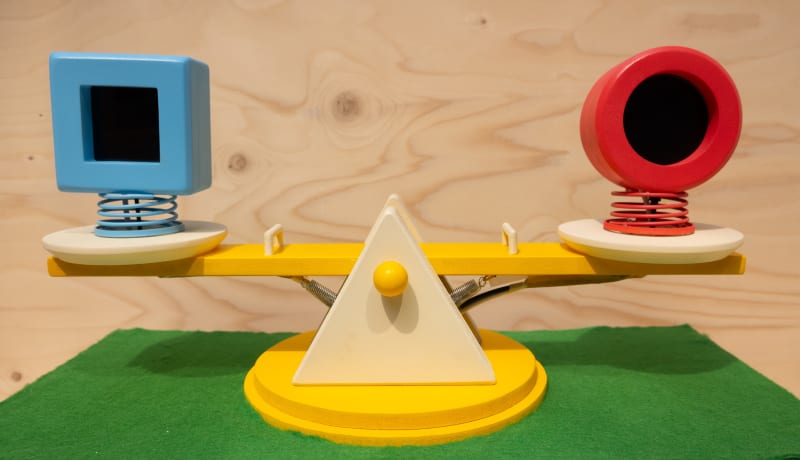 The seesaw features a blue square object on the left and a red circular object on the right, both mounted on springs. 