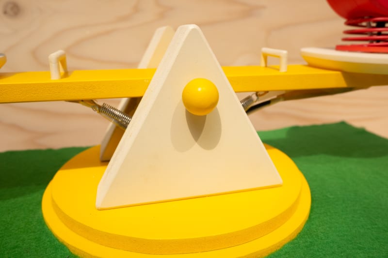 The seesaw features a blue square object on the left and a red circular object on the right, both mounted on springs. 