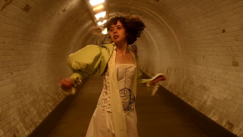 A woman in a Victorian inspired costume turns quickly to look behind herself in a dimly lit tunnel