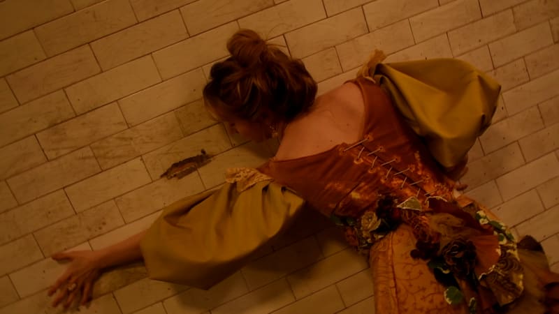 A woman in a yellow Victorian dress seems to grow from the walls of a tunnel.