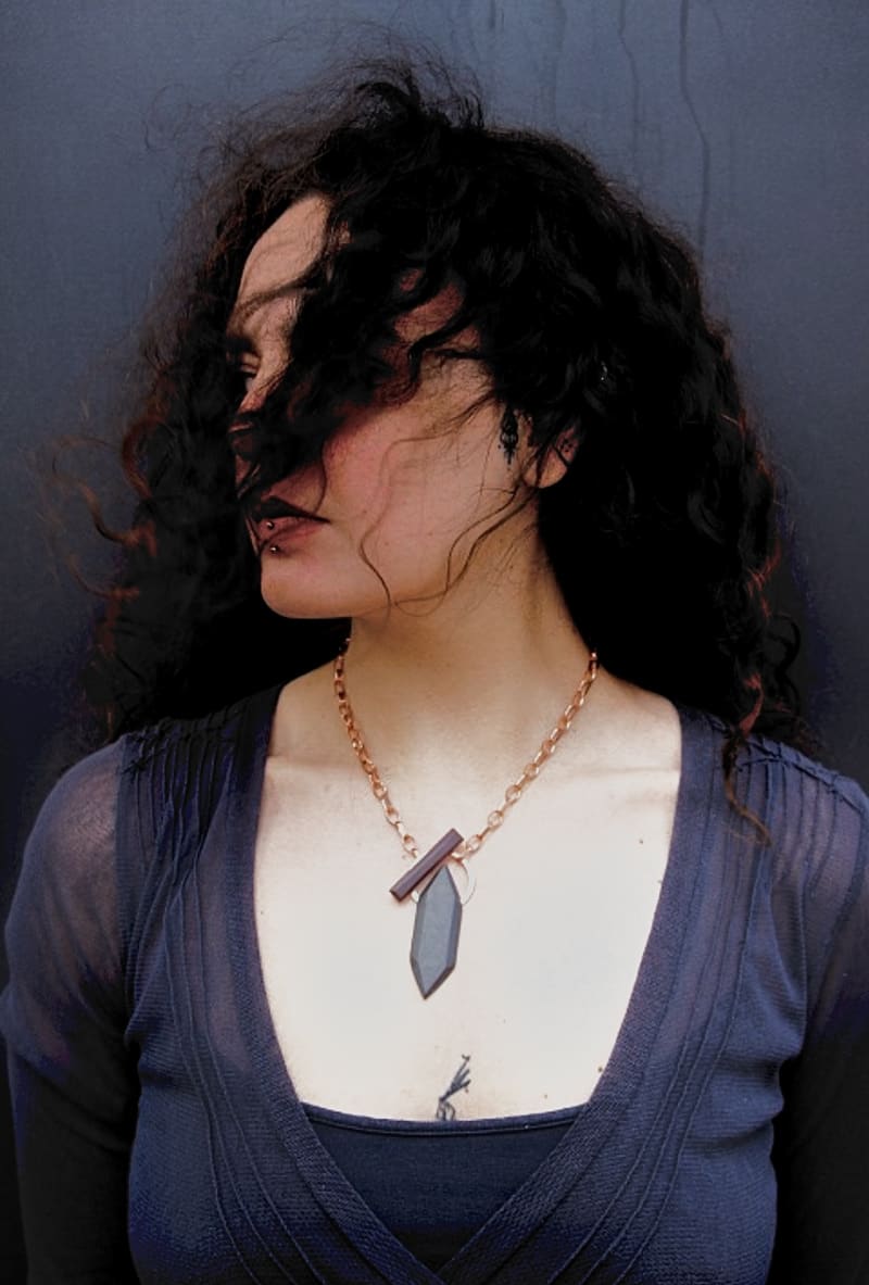 image 1: A woman with her blowing in her face wearing a necklace made of slate and copper. 