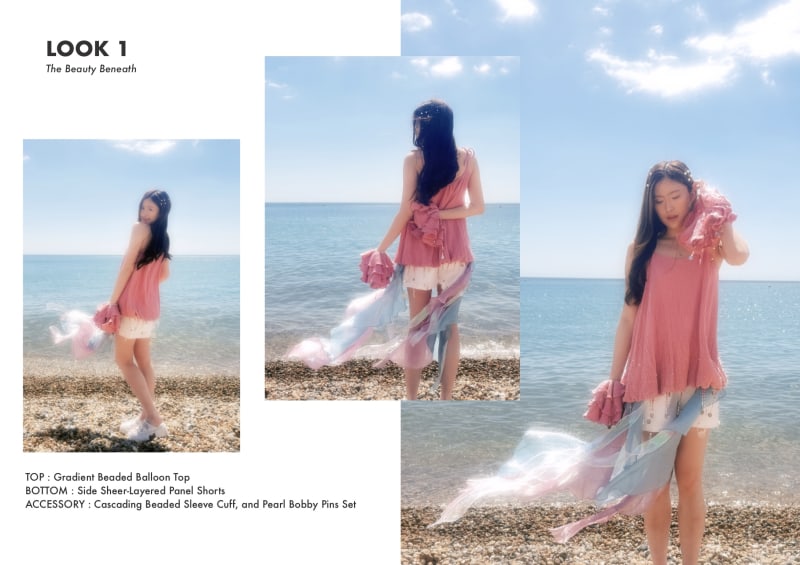 Model wearing balloon, beaded top and layered organza shorts, standing on a sunlit pebble beach with detailed description.