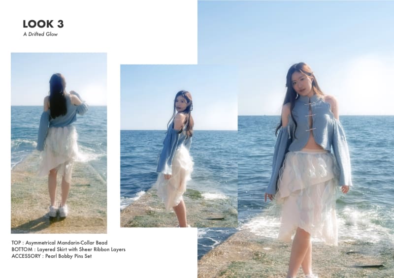 Model posing a a blue asymmetrical top with a sheer layered skirt, standing at the shore edge with detailed description.