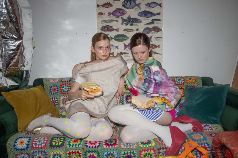models on a sofa wearing silk scarf over striped pinafore and oversized bread 