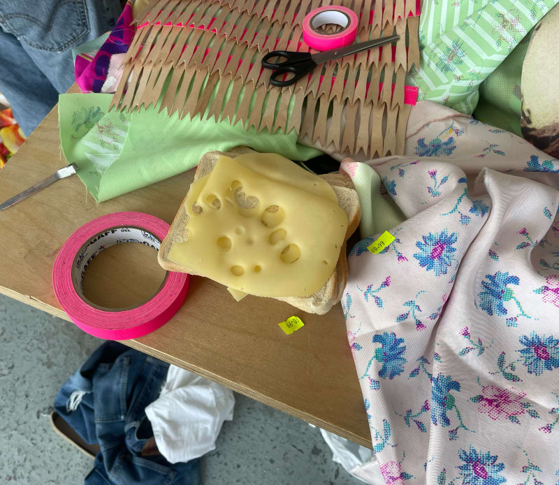 cluttered table with fabrics, scissors, bread and cheese 