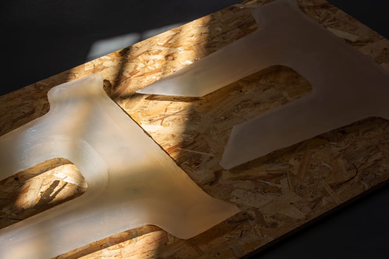 Sections of 2 anchor-like forms made out of soap, sat ontop of OSB wood, which has fragments gold leafed