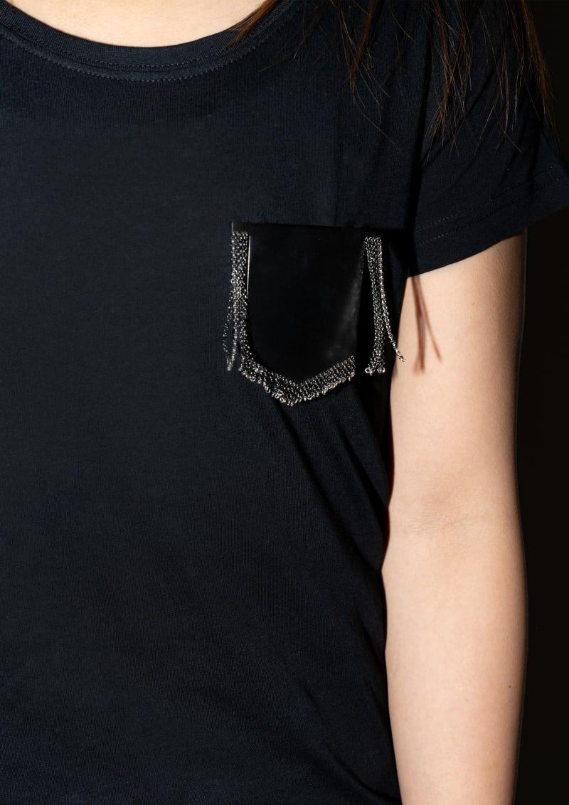 A silver shield-shaped brooch that mimics a black women's workwear T-shirt.