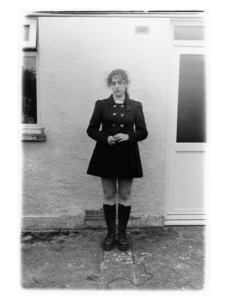 Black and white straight-up images of young woman in short black coat against a white textured wall. 
