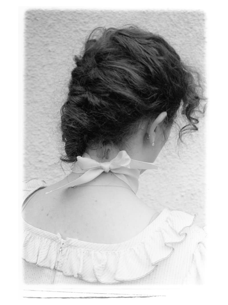 Black and white portrait taken of a young woman from behind, the focus drawn onto the bow tied around her neck.
