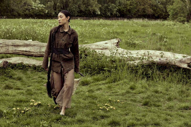 Very long shot of asian female model walking forward, wearing sheer brown skirt and suede khaki jacket. 
