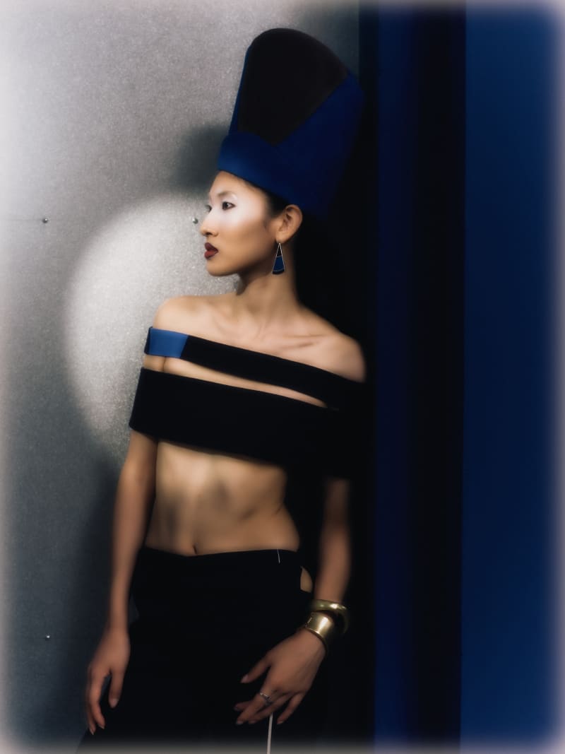 A woman in blue headpieces posing against a blue geometric background.