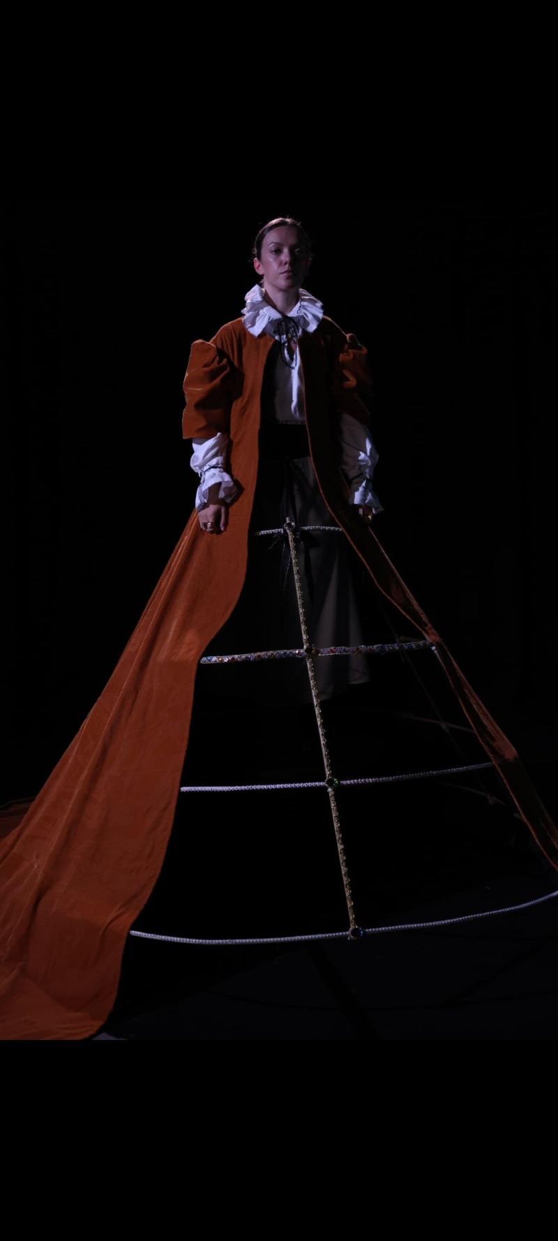 Image of a woman wearing a 16th century smock, jeweled farthingale, and orange velvet robe.