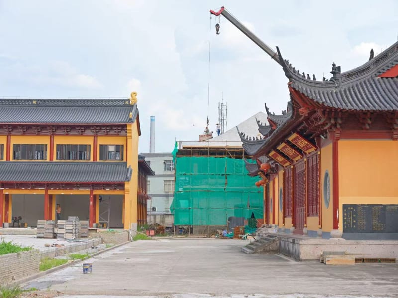 Yellow Buddhist temple buildings with a building surrounded by construction equipment and a crane.