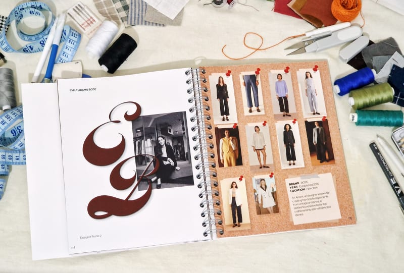 Open spiral-bound book showing fashion designer Emily Adams Bode’s profile and outfit images, surrounded by sewing tools, fabric swatches, threads.
