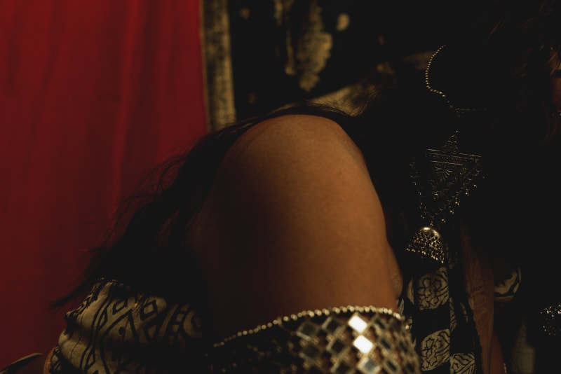 A woman in a saree and a kaleidoscope of traditional Indian jewelry from various parts of the region, posing infront of layers of Indian textiles.