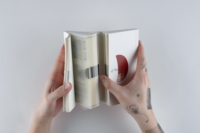 A person opens a white book titled Gate of Fortunes, revealing divination poems printed on both sides.