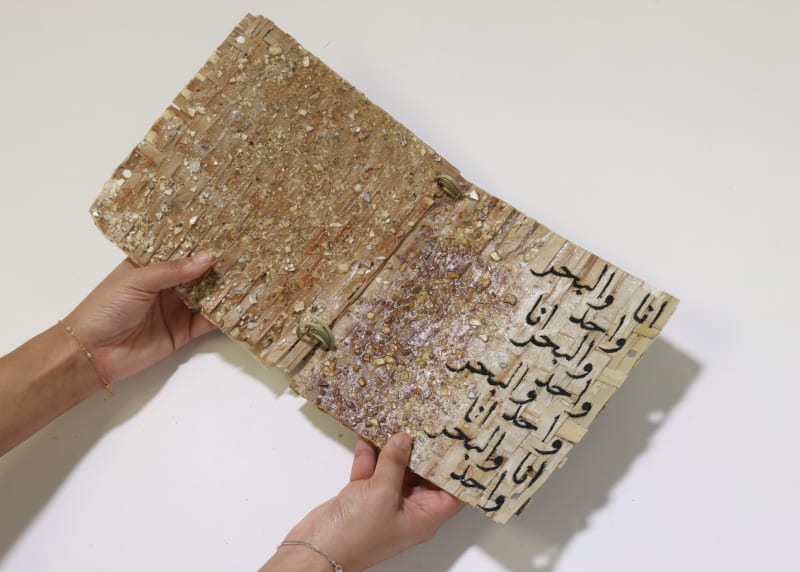 Woven palm leaf structures with embroidery of Arabic calligraphy 'the ocean and i are one' in a book format.