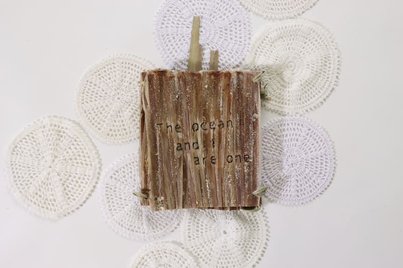 Palm leaf structure with embroidery of 'the ocean and i are one' in English in a book format.