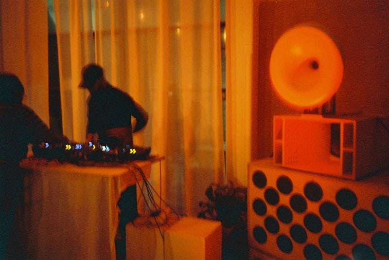 red/orange toned photographs of a group of people dancing and a DJ. Large white speakers