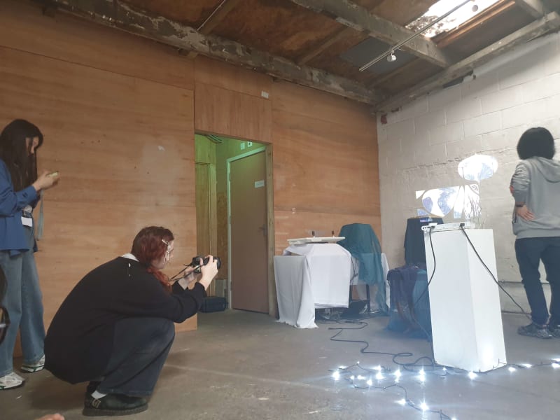 Three people in the installation space as it's being put togther. One is taking a photo of the space