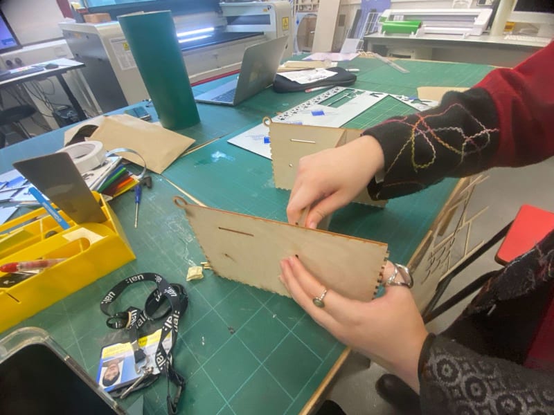 A pair of hands sticking pieces of wood together to form a box