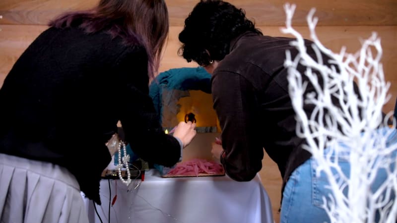 Two people looking into a box, with a figurine and papaer flowers