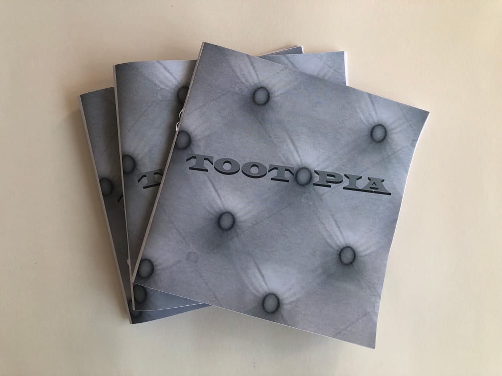 Image shows 3 zines layered on top of each other, the front cover is covered with a grey design which looks like the top of a mattress. The word TOOTOPIA is in bold across the page. 