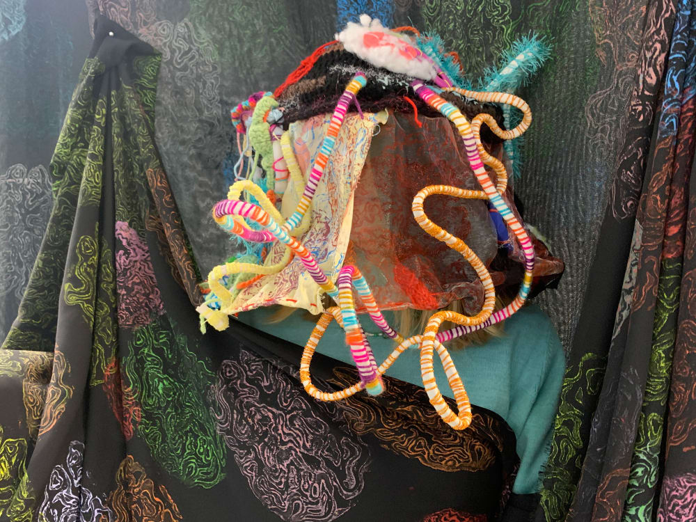Draped black cloth, printed with colourful brain scans hang with a 3D centre piece made to look like a brain with the intertwining of different textured materials and colours. 