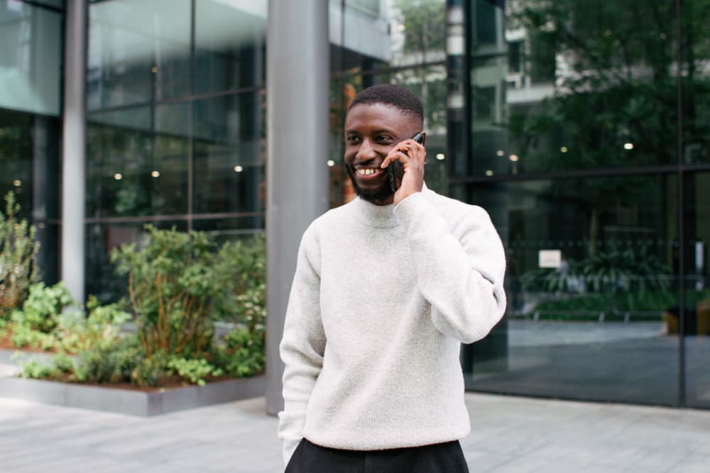 David's wearing a cream woollen jumper. He's stood outside talking on the phone