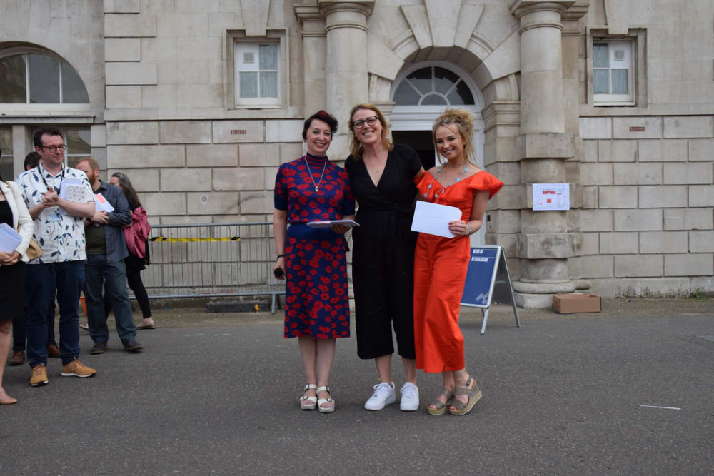 three women posing for a photo, one holding an envelope. 