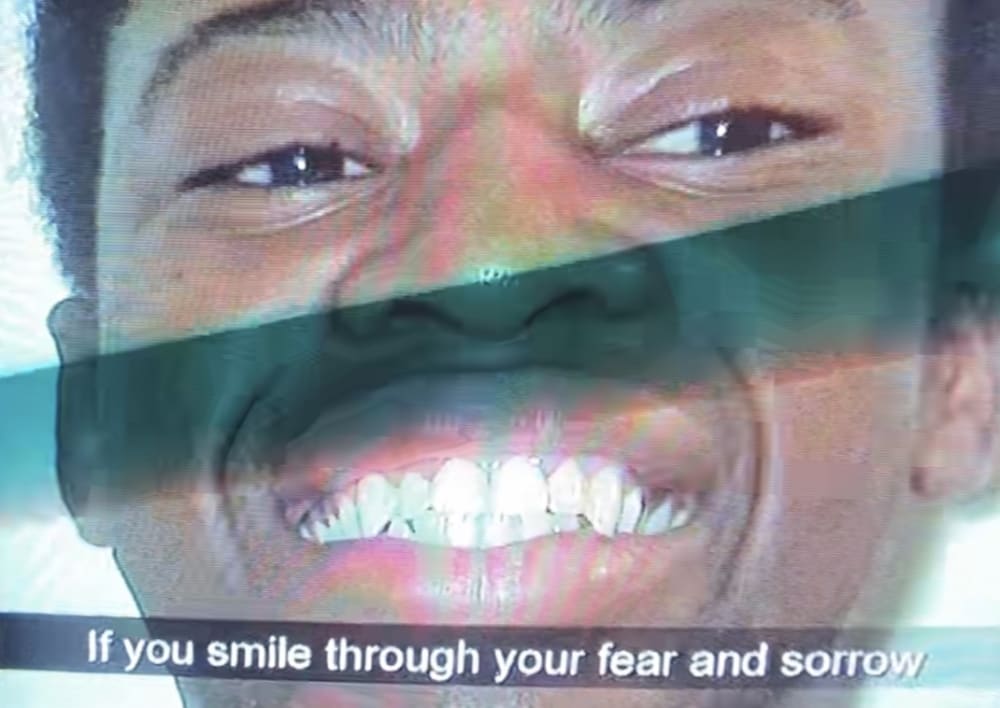 A man grimacing on a tv screen with the subtitles 'if you smile through your fear and sorrows'