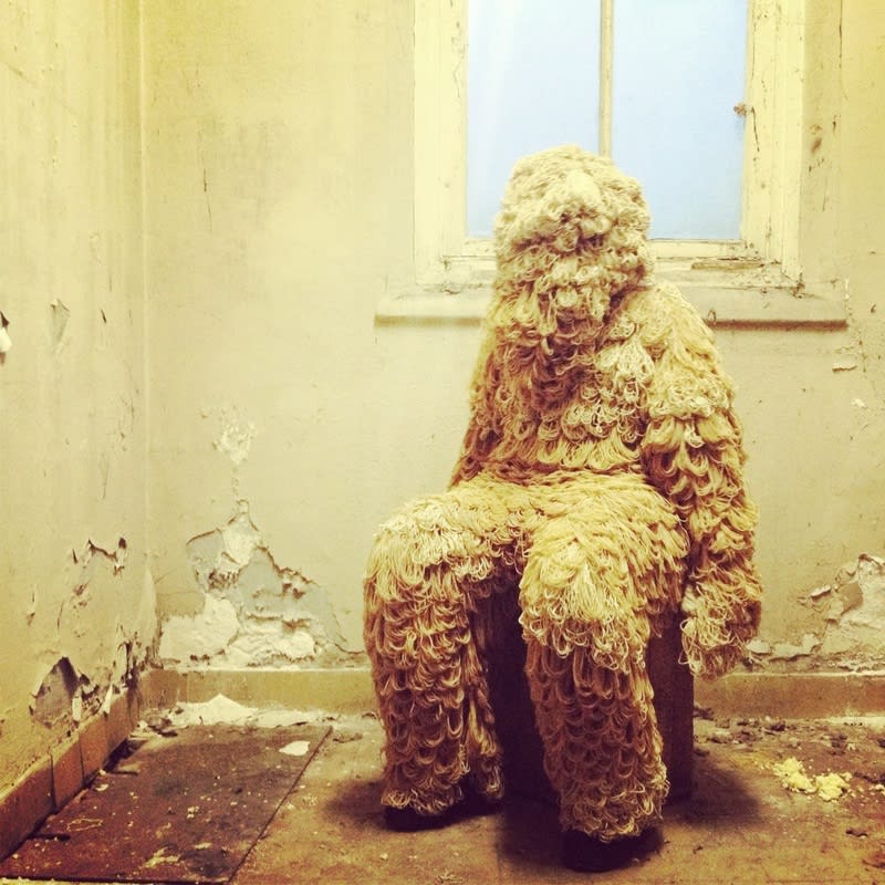 somebody sitting on a chair in a derelict house wearing an abstract outfit